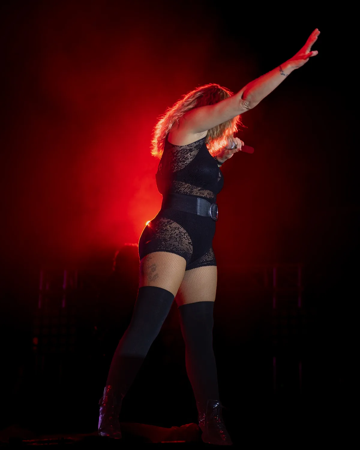 Dancer on stage with her arm raised under red light, at a concert in Balsicas